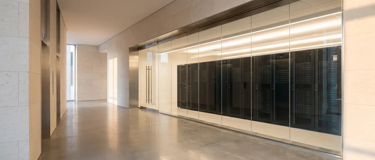 A pale limestone lobby with a long glass wall revealing rows of black server racks in soft light.