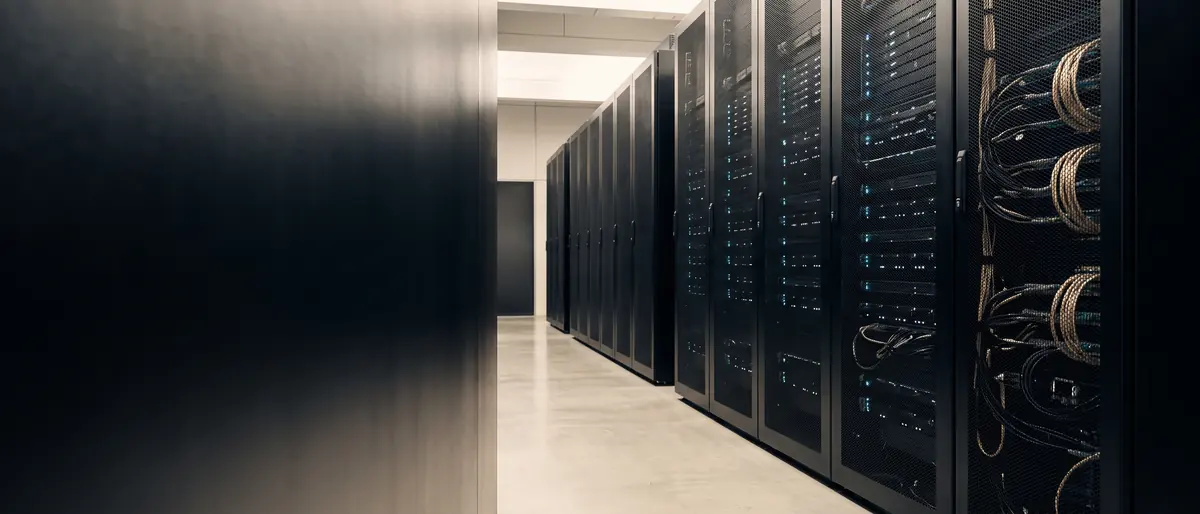 A quiet data centre aisle: rows of matte-black server racks with small status lights and neatly dressed cabling, beside a dark wall.